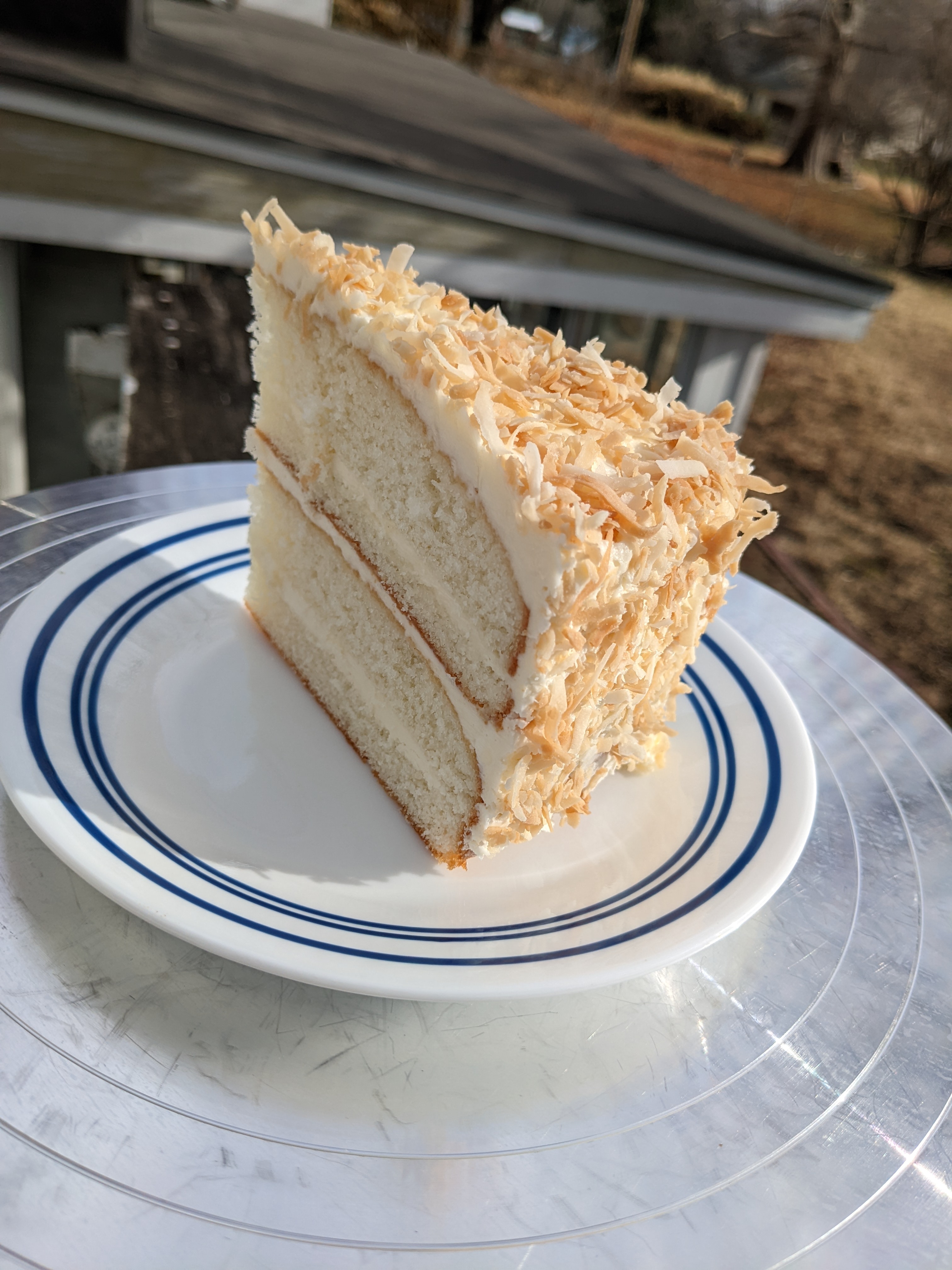 A slice of white cake with four layers, covered in tan and white coconut flakes.