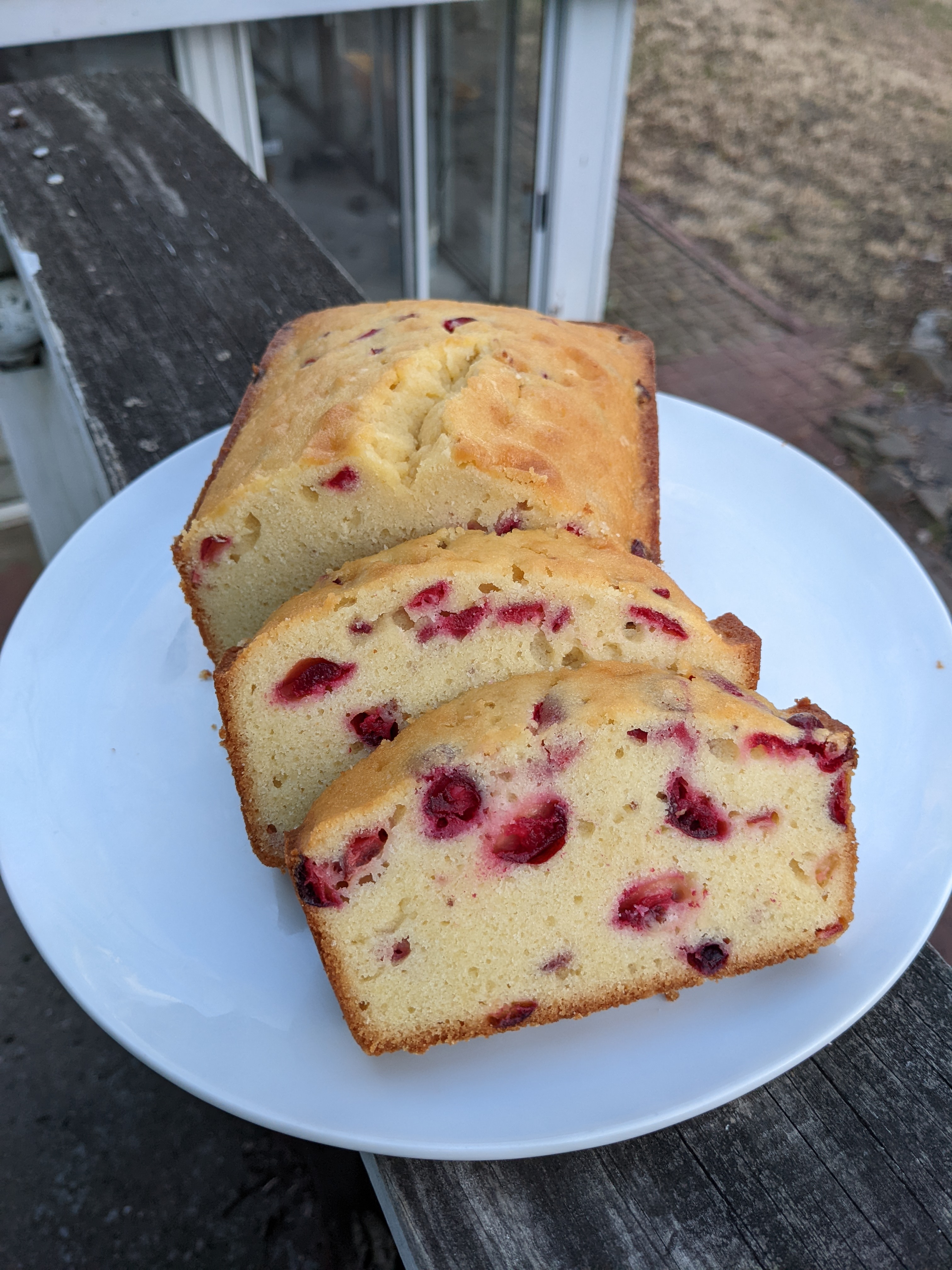 A loaf and two slices of pound cake dotted with red cranberries.